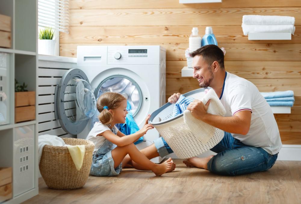 The laughing dad shows his daughter a laundry basket, they have a great time at the washing machine together