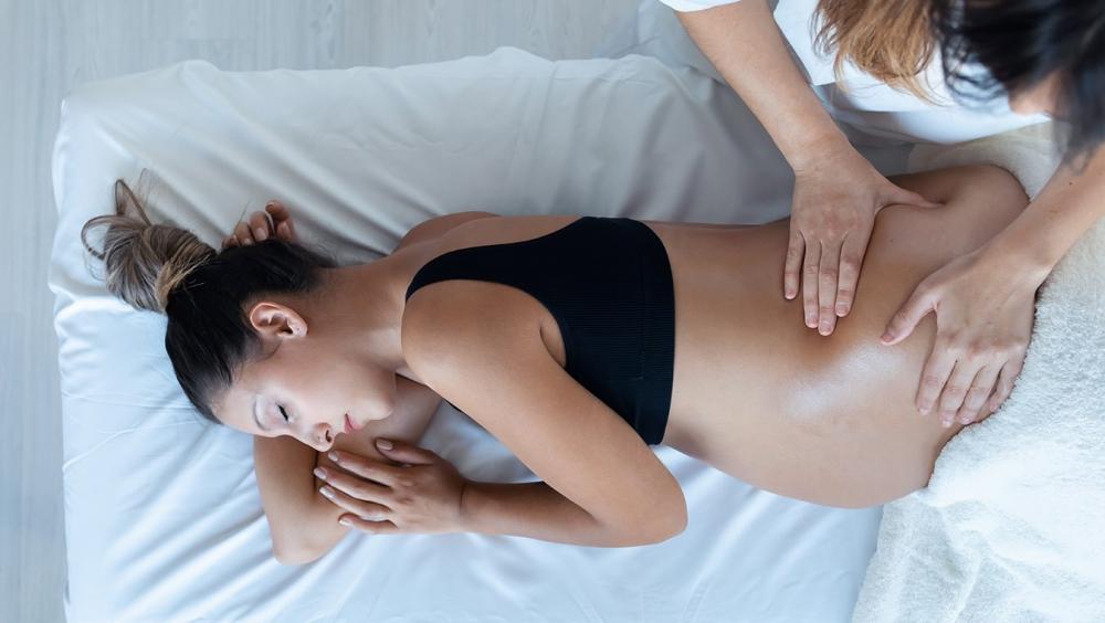 Pregnant woman laying on her side on the massage table, having her belly massaged by the physiotherapist
