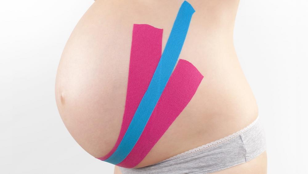 Pregnant woman's belly typed with colorful kinesiology tapes on white background