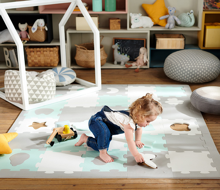 The 1.5-year-old girl is playing in her children's room on the Kinderkraft foam mat, arranging puzzles.