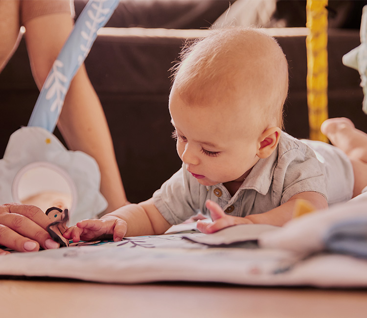 A baby is playing while lying on their stomach on the educational mat by Kinderkraft