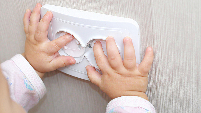 The baby's hands rest on the socket. It tries to stick its fingers in, but the socket has security features that prevent it.