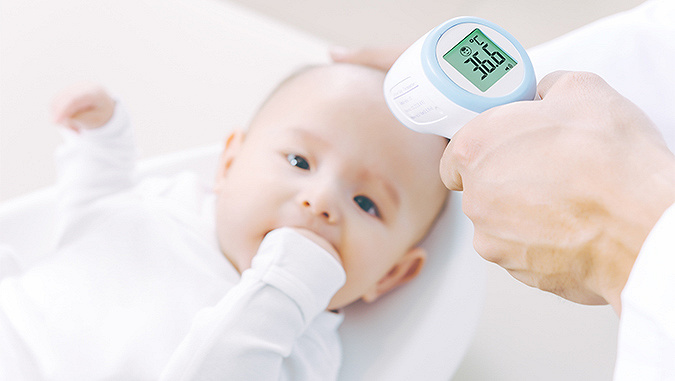 The baby lies at the doctor's and holds its own hand in its mouth. The doctor measures its temperature with a non-contact thermometer - it is 36.6°C.