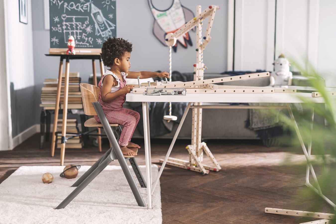 A little boy with black hair building a wooden structure; he's very focused and sitting in a Kinderkraft LIVY high chair