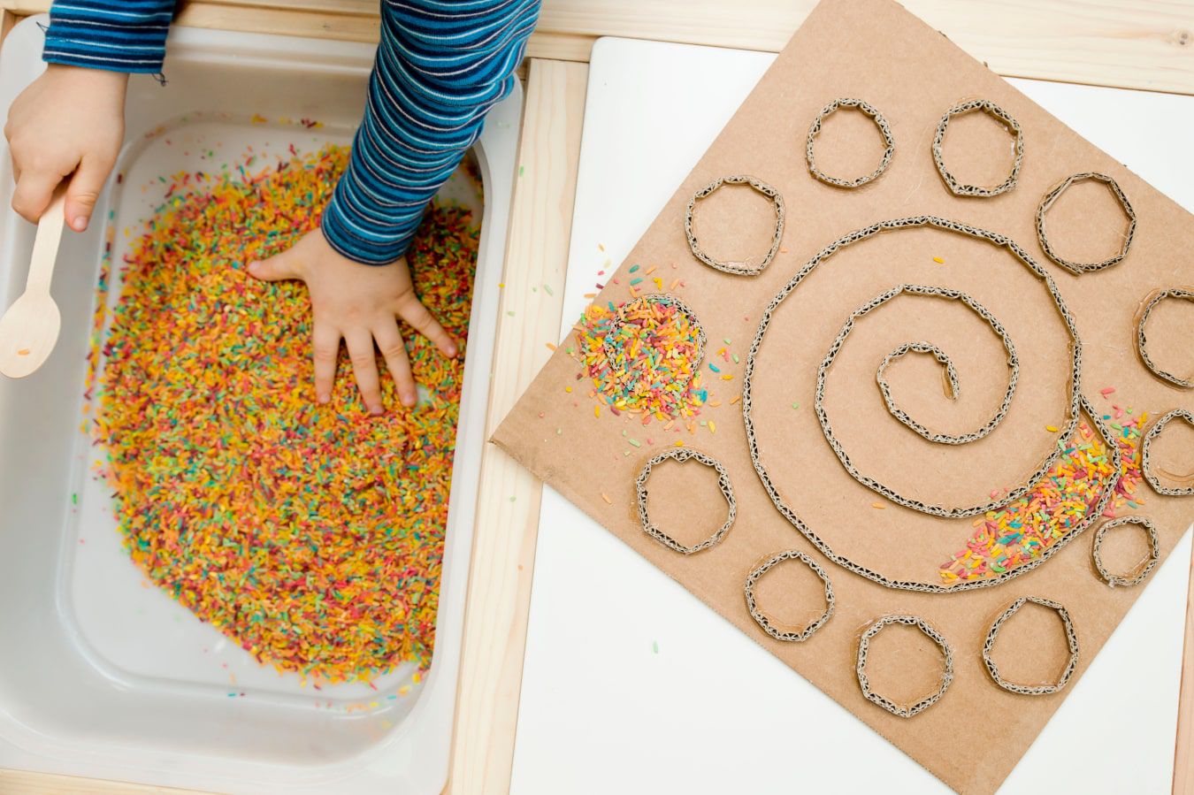 A child's hands learning a new texture – colourful lollies and sprinkles, next to this there's a DIY cardboard maze