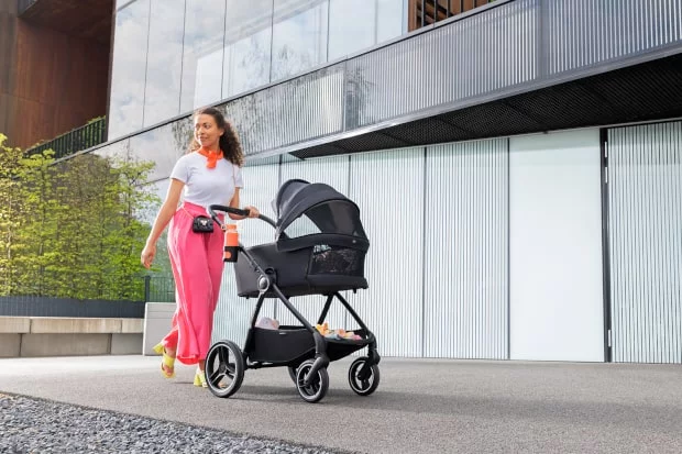 the woman is walking with a NEA stroller with additional ventilation. She smiles and walks in the city.