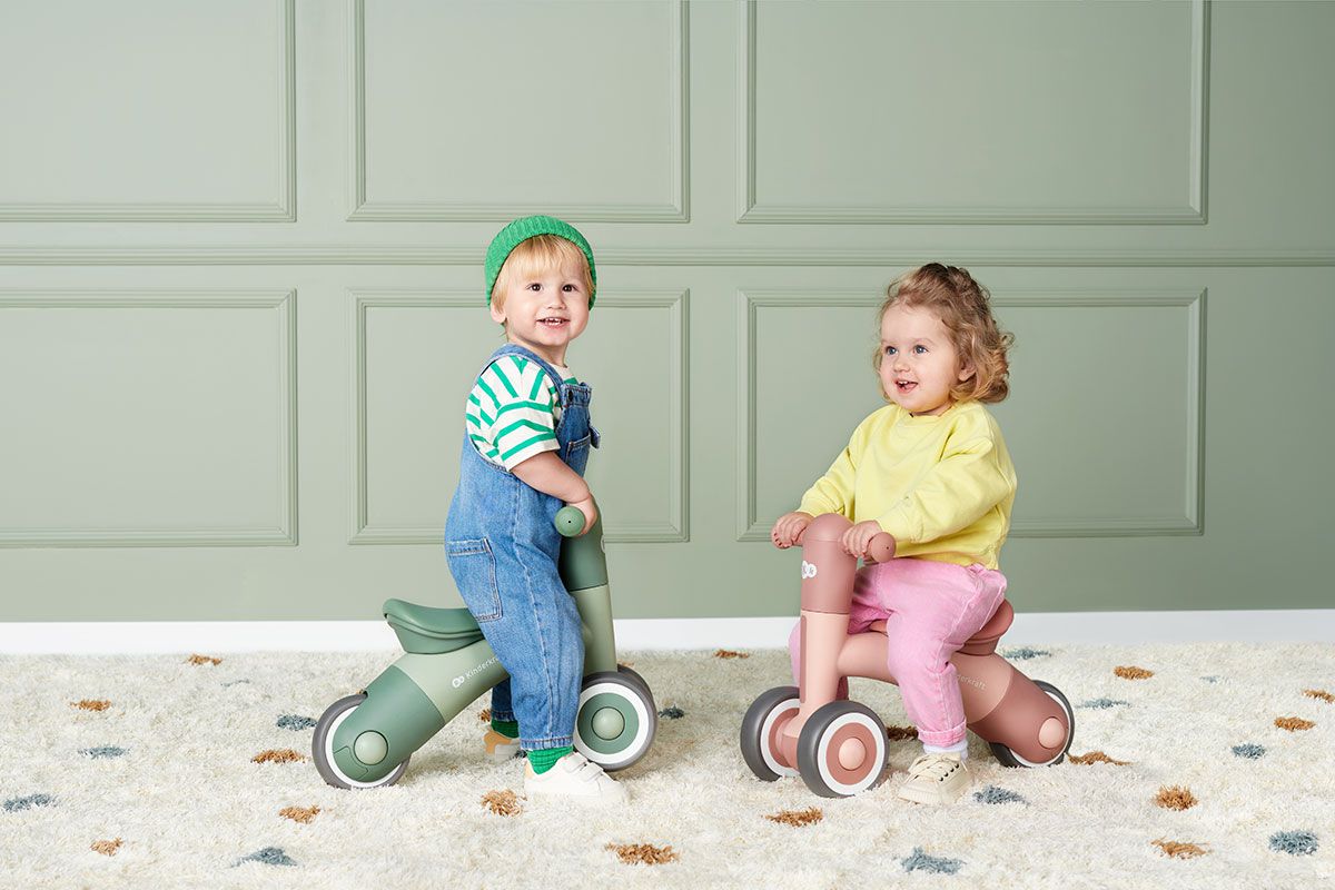 Two children sitting on MINIBI bikes playing on the carpet indoor. 