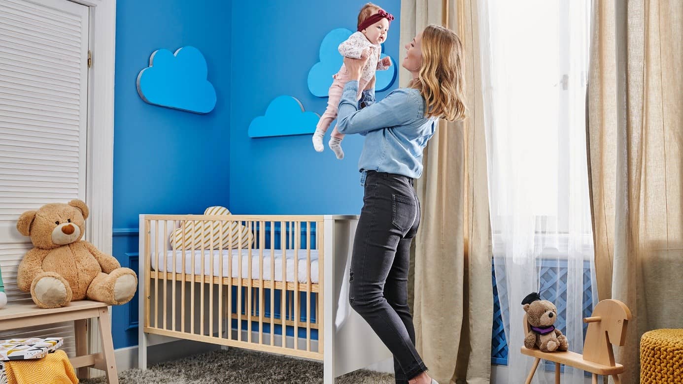 Mom is picking up her baby from the crib in the baby's room with blue walls