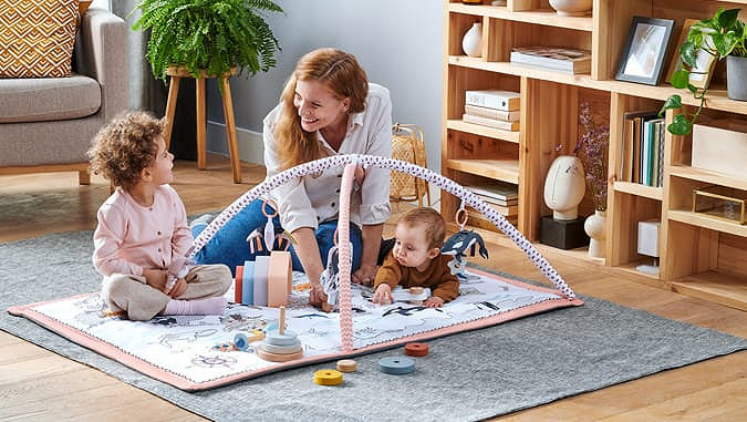 A mother with two children is playing on an educational mat inside the house