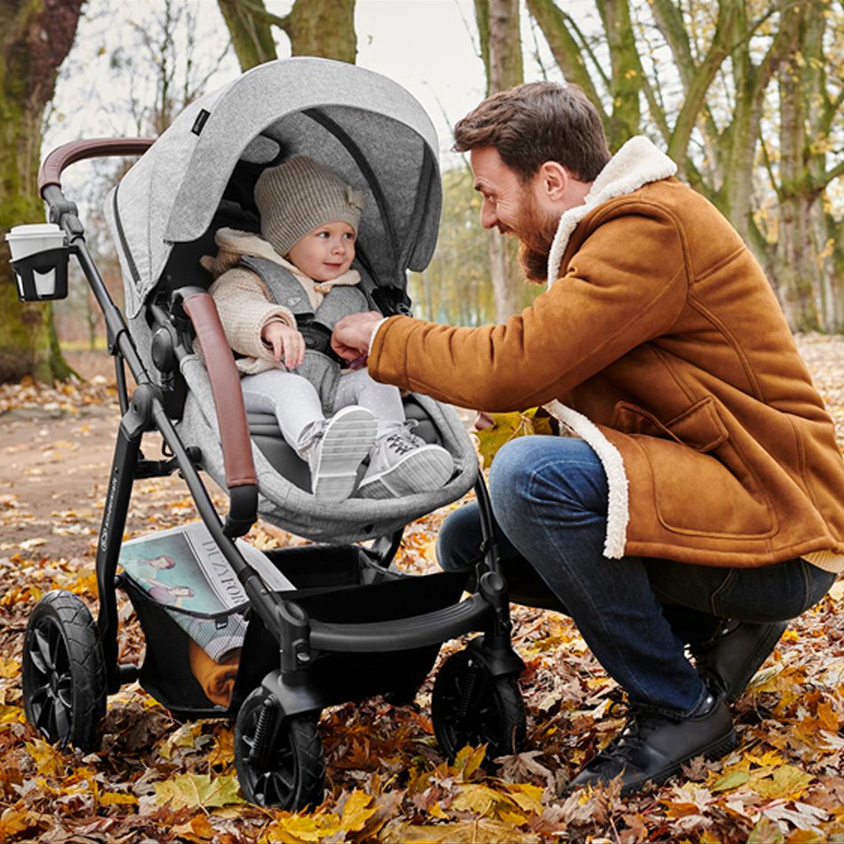 Dad in a jacket leans over to a baby sitting in a pushchair. The child is laughing, there are autumn leaves around