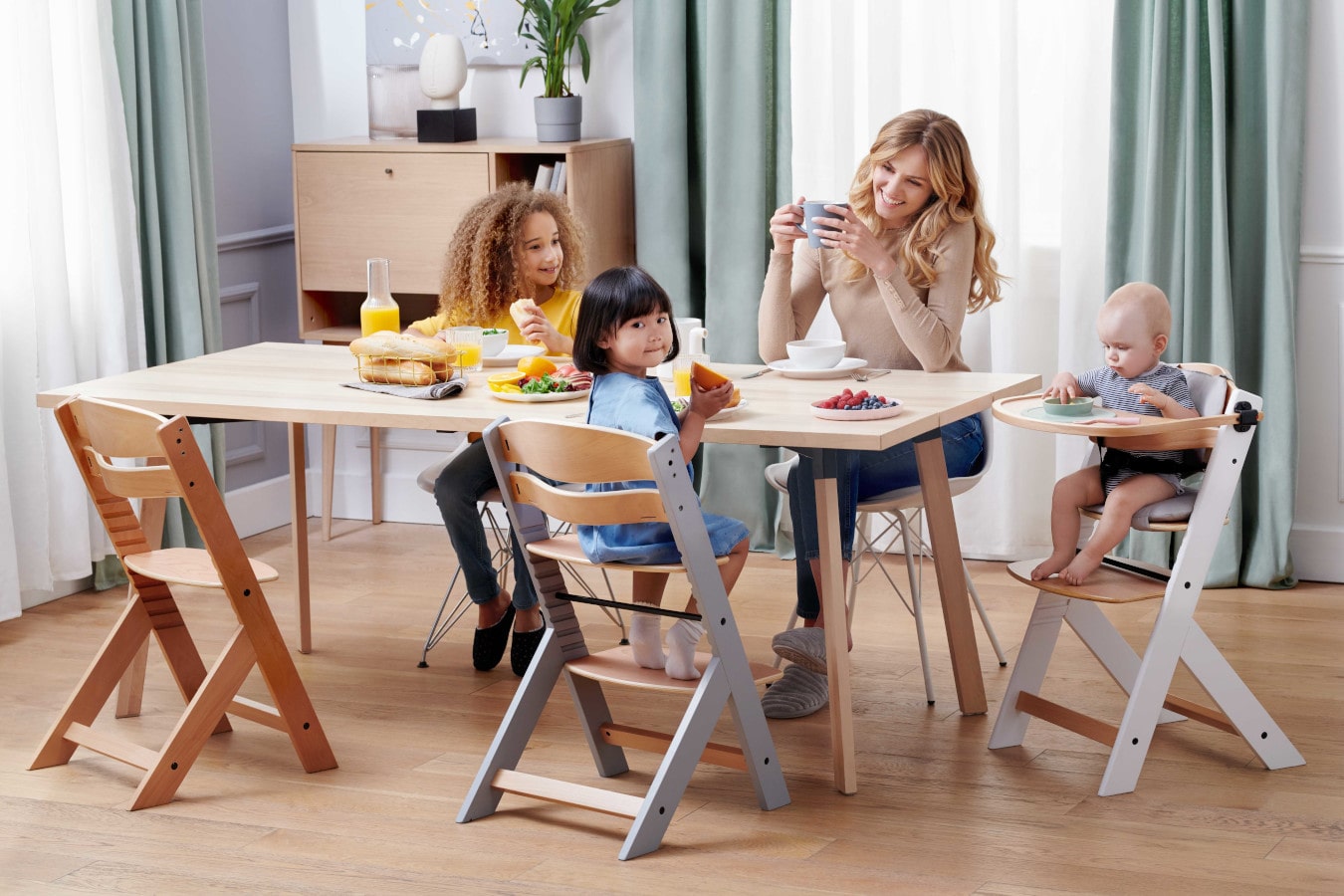 Mum and three children sitting at one table, mum is drinking a coffee and the children are happy. The ENOCK high chair has three available configurations – from a high chair to a chair for older children.