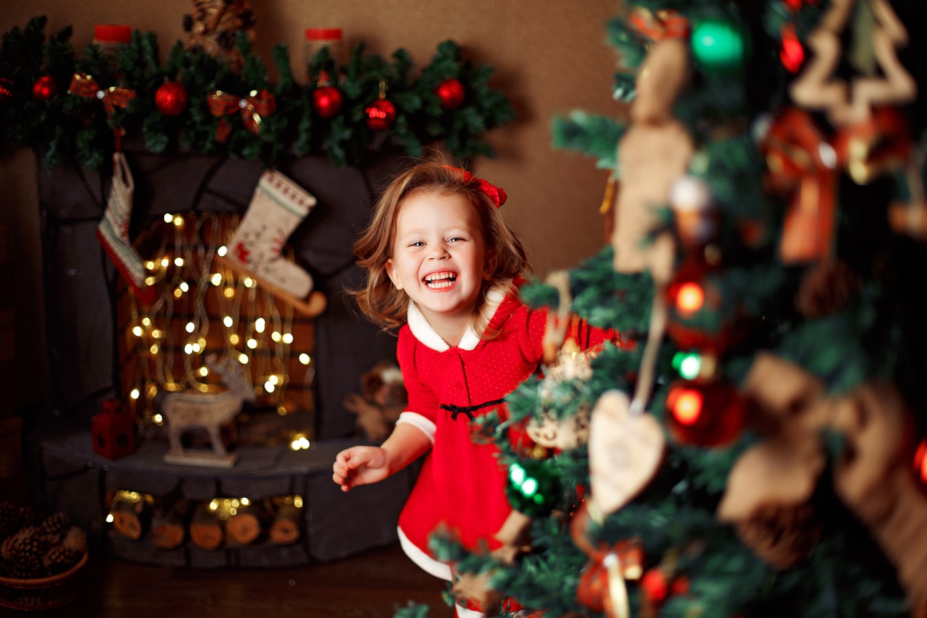 A happy girl in a red dress peeking out from behind a Christmas tree, laughing, happy